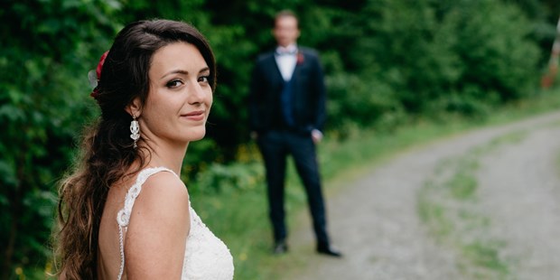 Hochzeitsfotos - Videografie buchbar - Lohnsburg - Braut mit Bräutigam im Hintergrund auf der Maierl-Alm in Kirchberg. WE WILL WEDDINGS | Hochzeitsfotografin Tirol / Wien - WE WILL WEDDINGS