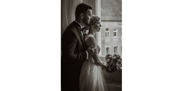 Hochzeitsfotos - Hemmingen (Region Hannover) - Im sanften Licht des Fensters des Ritterguts Ermlitz habe ich dieses stimmungsvolle Foto vom Bräutigam und der Braut eingefangen. Sie stehen nebeneinander, blicken nachdenklich in die Ferne. Der Bräutigam umarmt die Braut von hinten, eine Geste der Unterstützung und Zuneigung. Die Braut, mit ihrem eleganten Kleid und einem Strauß voller tiefblauer und cremefarbener Blumen, verkörpert die Anmut des Moments. Ihre Gesichter sind von einer ruhigen Vorfreude geprägt, als würden sie gemeinsam in ihre gemeinsame Zukunft schauen. Dieses Bild spiegelt die Intimität und das besondere Ambiente ihres Hochzeitstages wieder. - Mariana Siegert